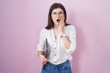 Wall Mural - Young caucasian woman holding laptop afraid and shocked, surprise and amazed expression with hands on face