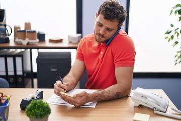 Sticker - Young hispanic man business worker talking on the smartphone write on document at office