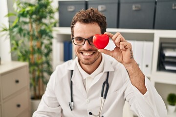 Sticker - Young hispanic man wearing doctor uniform holding heart at clinic