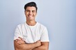 © Krakenimages.com - Hispanic man standing over blue background happy face smiling with crossed arms looking at the camera. positive person.