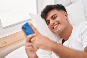 Sticker - Young hispanic man using smartphone lying on bed at bedroom