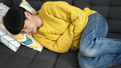 Wall Mural - Young chinese woman suffering for stomach ache lying on sofa at home