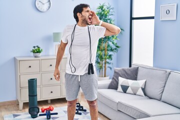 Canvas Print - Handsome latin man wearing sportswear at home shouting and screaming loud to side with hand on mouth. communication concept.