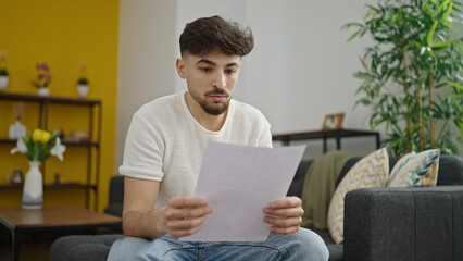 Wall Mural - Young arab man reading paper sitting on sofa at home