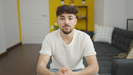 Sticker - Young arab man sitting on sofa with relaxed expression at home