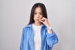 Young chinese woman standing over white background mouth and lips shut as zip with fingers. secret and silent, taboo talking