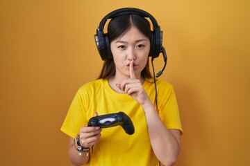 Poster - Chinese young woman playing video game holding controller asking to be quiet with finger on lips. silence and secret concept.