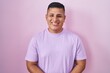 © Krakenimages.com - Young hispanic man standing over pink background with hands together and crossed fingers smiling relaxed and cheerful. success and optimistic