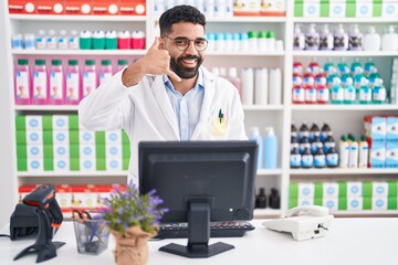 Poster - Hispanic man with beard working at pharmacy drugstore smiling doing phone gesture with hand and fingers like talking on the telephone. communicating concepts.