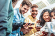 © Davide Angelini - Diverse group of young people using smart mobile phone device outside - University students watching cellphone in college campus - Happy teenagers addicted to social media - Technology concept