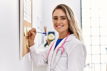 Wall Mural - Young woman wearing doctor uniform writing on corkboard at clinic