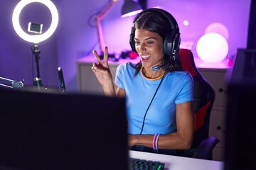 Wall Mural - Brunette young woman playing video games smiling with happy face winking at the camera doing victory sign. number two.