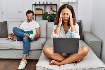 Poster - Hispanic middle age couple at home, woman using laptop with hand on head for pain in head because stress. suffering migraine.