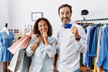 Canvas Print - Hispanic middle age couple holding shopping bags and credit card with hand on chin thinking about question, pensive expression. smiling and thoughtful face. doubt concept.