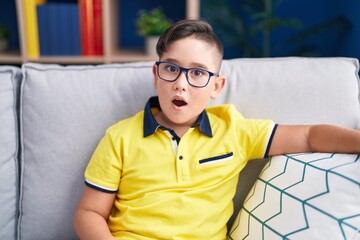 Canvas Print - Young hispanic kid sitting on the sofa at home scared and amazed with open mouth for surprise, disbelief face