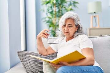 Sticker - Middle age woman reading book sitting on sofa at home