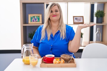 Poster - Caucasian plus size woman eating breakfast at home smiling cheerful presenting and pointing with palm of hand looking at the camera.