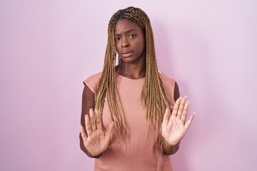 Wall Mural - African american woman with braided hair standing over pink background moving away hands palms showing refusal and denial with afraid and disgusting expression. stop and forbidden.