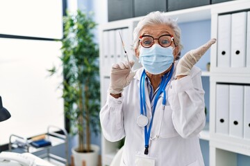 Wall Mural - Senior woman with grey hair wearing doctor uniform and medical mask holding syringe celebrating victory with happy smile and winner expression with raised hands