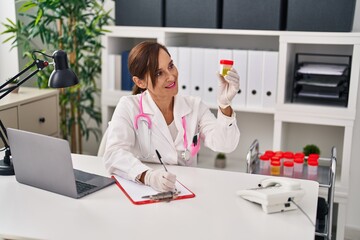 Canvas Print - Middle age woman wearing doctor uniform holding urine analysis test tube at clinic