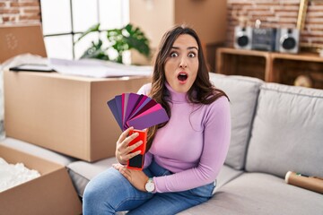 Sticker - Young brunette woman moving to a new home choosing wall painting scared and amazed with open mouth for surprise, disbelief face