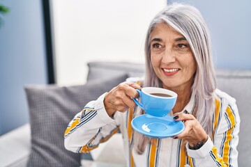 Poster - Middle age grey-haired woman drinking coffee sitting on sofa at home