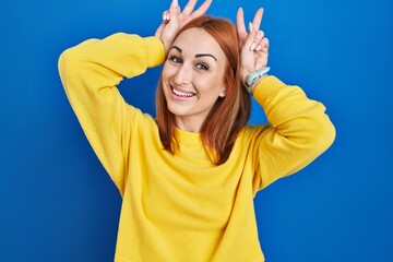 Sticker - Young woman standing over blue background posing funny and crazy with fingers on head as bunny ears, smiling cheerful