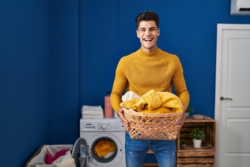 Poster - Young hispanic man holding laundry basket smiling and laughing hard out loud because funny crazy joke.