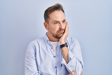 Poster - Middle age caucasian man standing over blue background thinking looking tired and bored with depression problems with crossed arms.