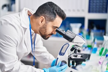 Wall Mural - Young hispanic man scientist using microscope at laboratory