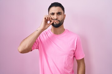 Wall Mural - Hispanic young man standing over pink background mouth and lips shut as zip with fingers. secret and silent, taboo talking