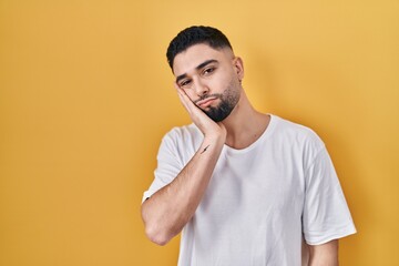 Wall Mural - Young handsome man wearing casual t shirt over yellow background thinking looking tired and bored with depression problems with crossed arms.