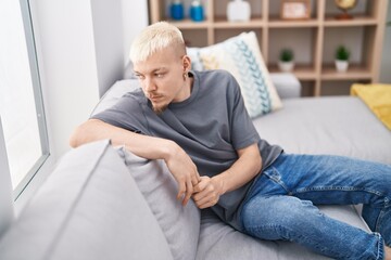 Wall Mural - Young caucasian man sitting on sofa with serious expression at home