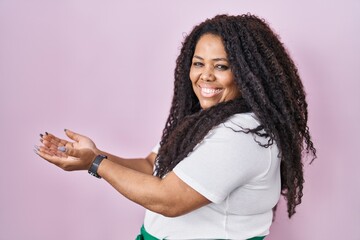 Poster - Plus size hispanic woman standing over pink background pointing aside with hands open palms showing copy space, presenting advertisement smiling excited happy