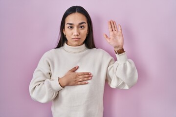 Poster - Young south asian woman standing over pink background swearing with hand on chest and open palm, making a loyalty promise oath