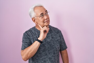 Wall Mural - Middle age man with grey hair standing over pink background with hand on chin thinking about question, pensive expression. smiling with thoughtful face. doubt concept.