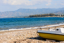 A Lonely Yellow Boat Stands On The Rocky Shore Of The Mediterranean Blue Sea. Travel Mood On A Sunny Day