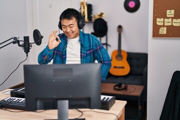 Sticker - Young chinese man looking at online music tutorial doing ok sign with fingers, smiling friendly gesturing excellent symbol