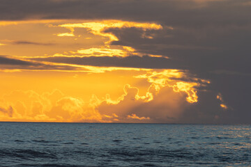 Wall Mural - A sea at sunset and sun breaking through dark gray clouds