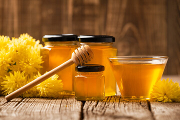 Wall Mural - Honey in bowls, dipper and flowers on an aged wooden background.