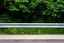 Sidewalk, Highway Guard Rail, Green Grass And Bushes