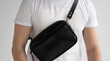 Man in a white t-shirt with a leather black handmade bag over his shoulder. Dark designer banana bag. Comfortable small bag for walking.