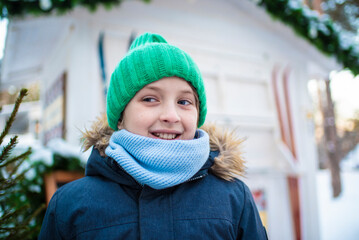 Wall Mural - miling boy with green cap in snowy winter at fair, festival	