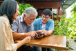 © CandyRetriever  - Happy Asian couple teaching elderly father using mobile phone application during having lunch together at restaurant on summer vacation. Family relationship older people mental health care concept.