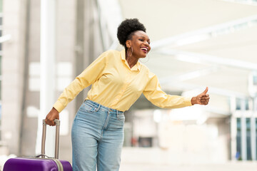 Wall Mural - Cheerful Black Female Tourist Catching Taxi With Gesture At Airport