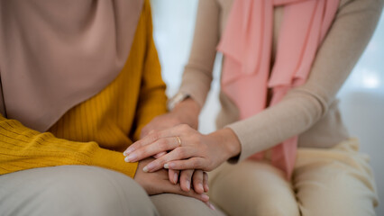 Close up Asian woman and friends sitting on couch two people holding hands. trusted friend, true friendship concept.