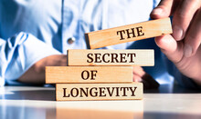 Close Up On Businessman Holding A Wooden Block With "The Secret Of Longevity" Message