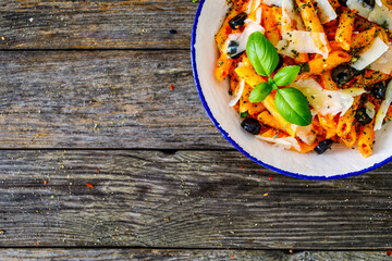 Noodles with pesto, parmesan cheese, basil and black olives served on wooden table