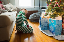 Elementary Age Boy Looks Sideways At Christmas Presents Under The Tree