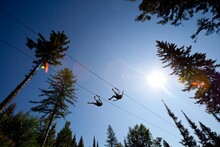 Two People Ride A Zip Line In Whitefish, Montana.
